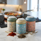 MARIA ROMA Botanica spice jar set with gold spoons featuring paprika, black pepper, and rock salt next to a cooking pan on a modern induction cooktop."
